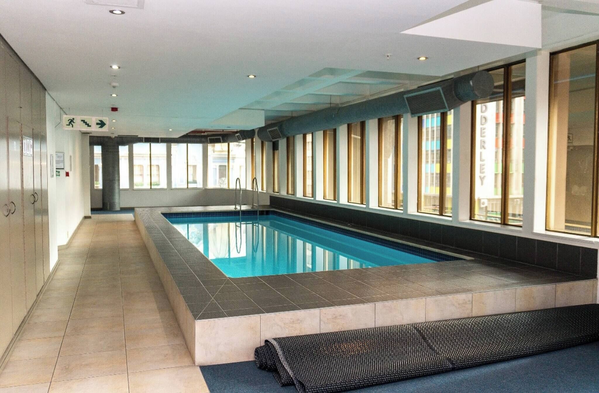 Una piscina amb sòl de rajola, paret de vidre i un passadís amb finestres.