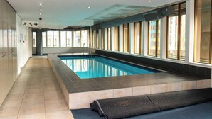 Una piscina con suelo de baldosas, pared de vidrio y un corredor con ventanas.