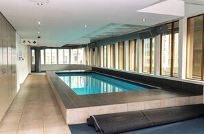 Ein Schwimmbecken mit gefliestem Boden, einer Glaswand und einem Gang mit Fenstern.
