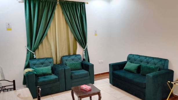 A living room with two green sofas, a wooden coffee table, and a dining table. - Quiet Room 10 (Riyadh)