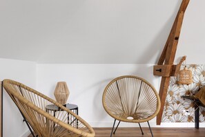Quarto com duas cadeiras de vime, uma mesa pequena e uma estrutura de madeira fixada na parede.