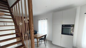 A modern kitchen with white cabinets, a wooden staircase, and a dining area with a table and chairs.