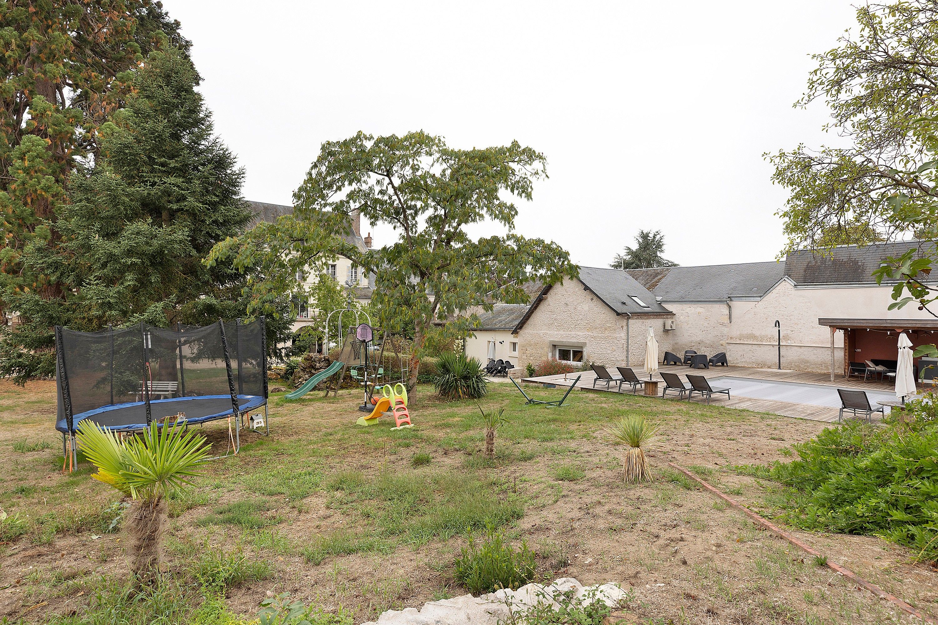 A residential backyard with a trampoline, playset, and outdoor seating area.