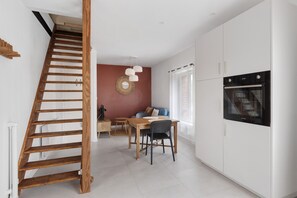 A modern kitchen with white cabinets, a wooden staircase, and a dining area with a table and chairs. - Gite "La Glycine" for 2 with Heated Pool from Mid-May to September (Veuzain-sur-Loire)