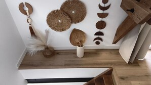 A staircase with a wooden finish, a white wall with decorative wall hangings, and a white vase with a feather arrangement.