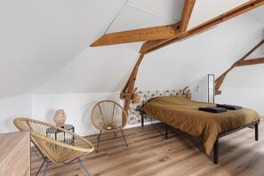 A bedroom with a sloped ceiling, a bed, two wicker chairs, and a small table. - Gite "La Glycine" for 2 with Heated Pool from Mid-May to September (Veuzain-sur-Loire)