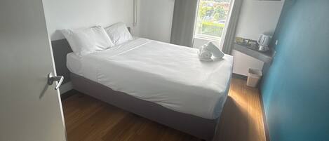 Een slaapkamer met een bed, een raam, een bureau en een stoel.