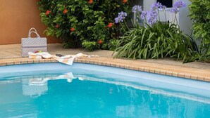 Una piscina con una bolsa y toallas en el borde, rodeada de follaje y flores.