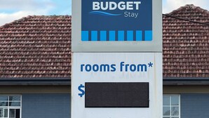 Un cartel anuncia habitaciones económicas en Coffs Harbour con servicios como camas cómodas, desayuno excelente y WiFi gratuito.