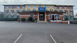 Un hotel de varios pisos con entrada central, unidades de aire acondicionado y un letrero que dice 'BUDGET Stay'.