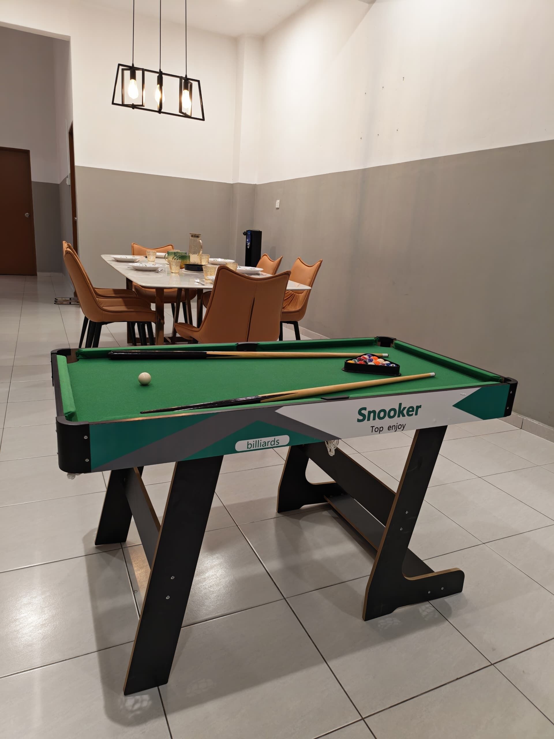 Un tavolo da biliardo con l'etichetta 'Snooker', un tavolo da pranzo con sedie e un lampadario.