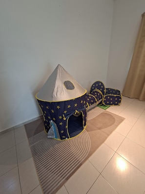 A play tent with a star pattern and a small window, placed on a patterned rug in a room with tiled flooring.