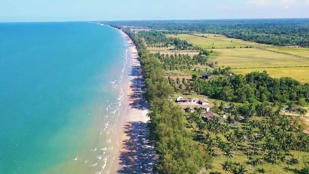 An aerial view of a coastal area with a beach, adjacent fields, and scattered buildings. - Kuantan putra home (Kuala Lipis)