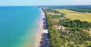 Vista aérea de uma área costeira com praia, campos vizinhos e edifícios dispersos.