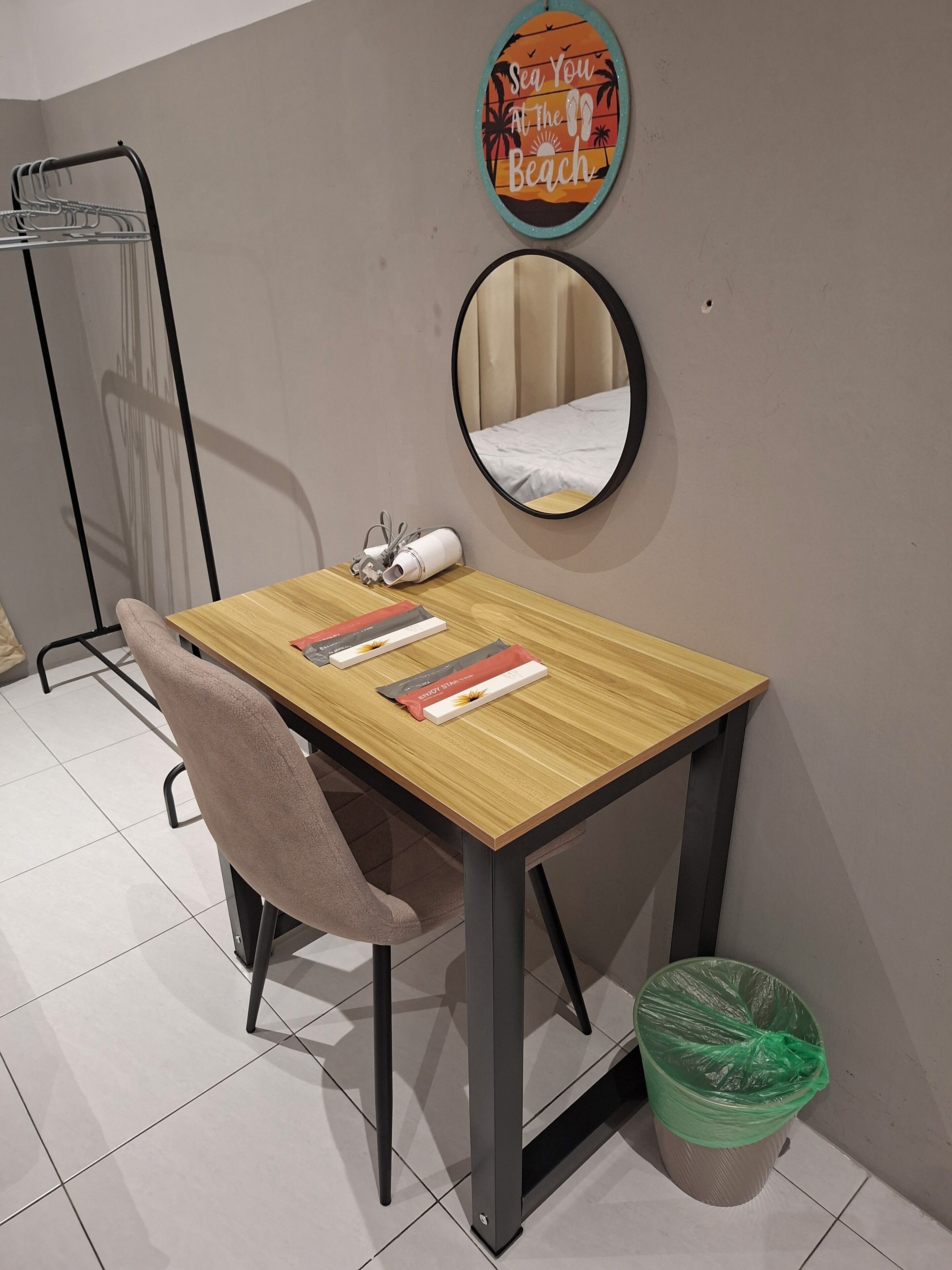 Een kamer met een houten tafel, een stoel, een spiegel, een handdoekhouder en een prullenbak.