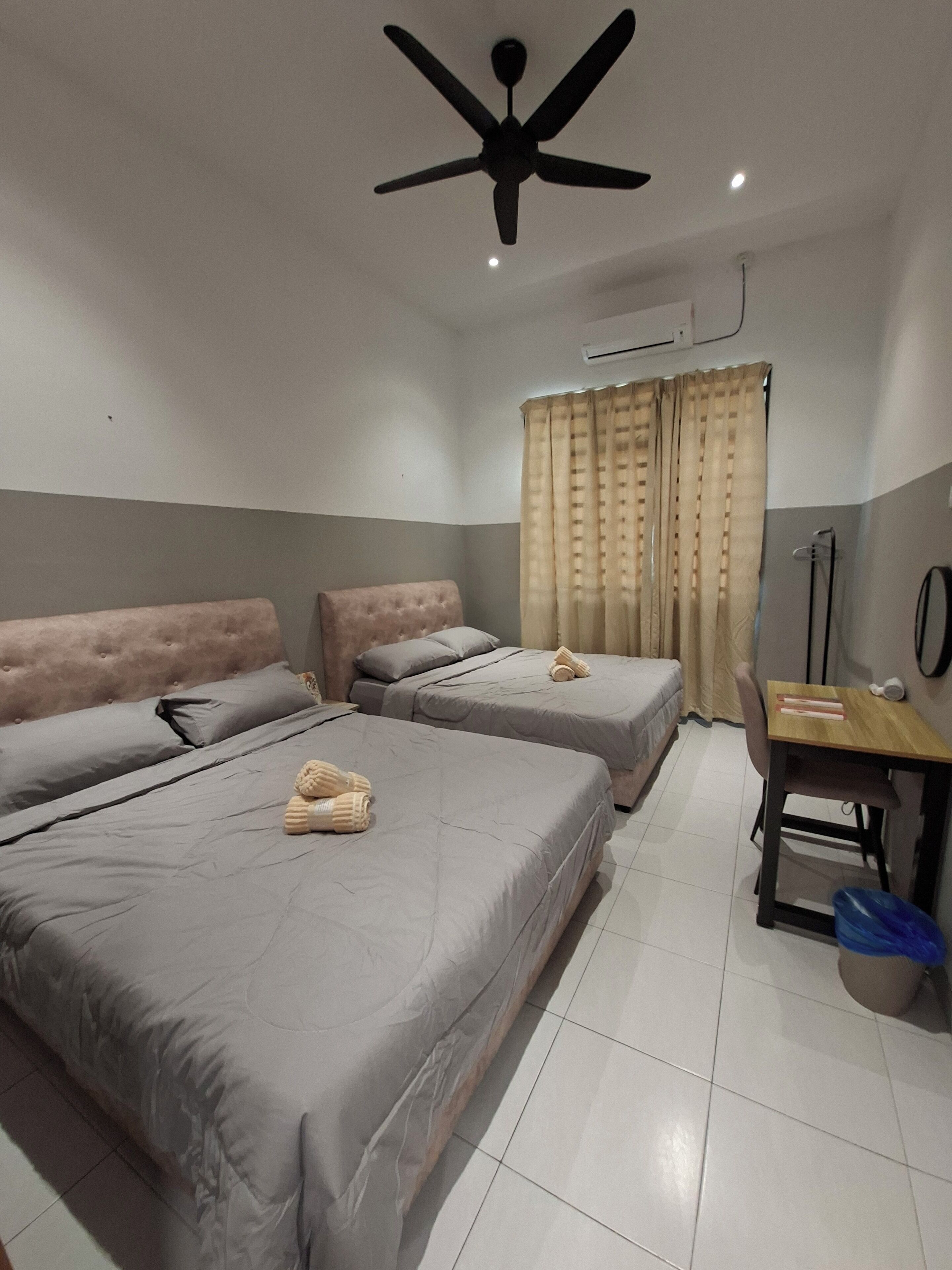 A hotel room with two beds, a ceiling fan, a desk with a chair, and a window with curtains.
