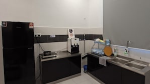 A modern kitchen with a black refrigerator, a coffee machine, a sink, and a tiled backsplash. - Kuantan putra home (Kuala Lipis)