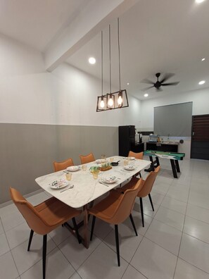 Un comedor con una mesa rectangular, sillas anaranjadas, un ventilador de techo y una mesa de billar.