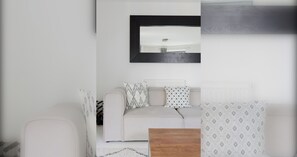 Ein modernes Wohnzimmer mit einem weißen Sofa, gemusterten Kissen, einem Holztisch und einem Spiegel über dem Sofa.