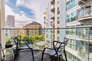 A balcony with two chairs and a small table, overlooking a cityscape with modern buildings. - Sophisticated 2BD Flat with Riverside Views (Greater London)
