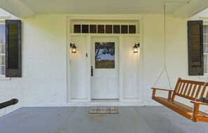 A white building with a front door, two wall-mounted lanterns, a wooden bench, and a welcome mat. - This house is a 3 bedroom(s), 2 bathrooms, located in Frankfort, KY. (Frankfort)