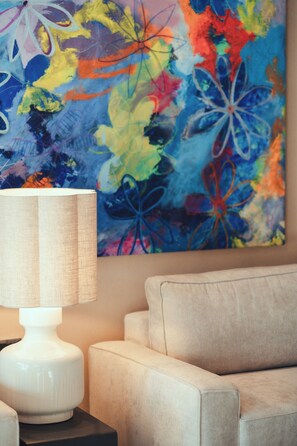 Ein Zimmer mit einem beigen Sofa, einer weißen Lampe und einem farbenfrohen, abstrakten Gemälde an der Wand.