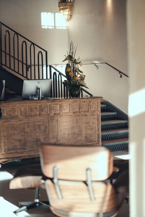 Un comptoir d’accueil avec un ordinateur, un vase de fleurs et un escalier en arrière-plan.