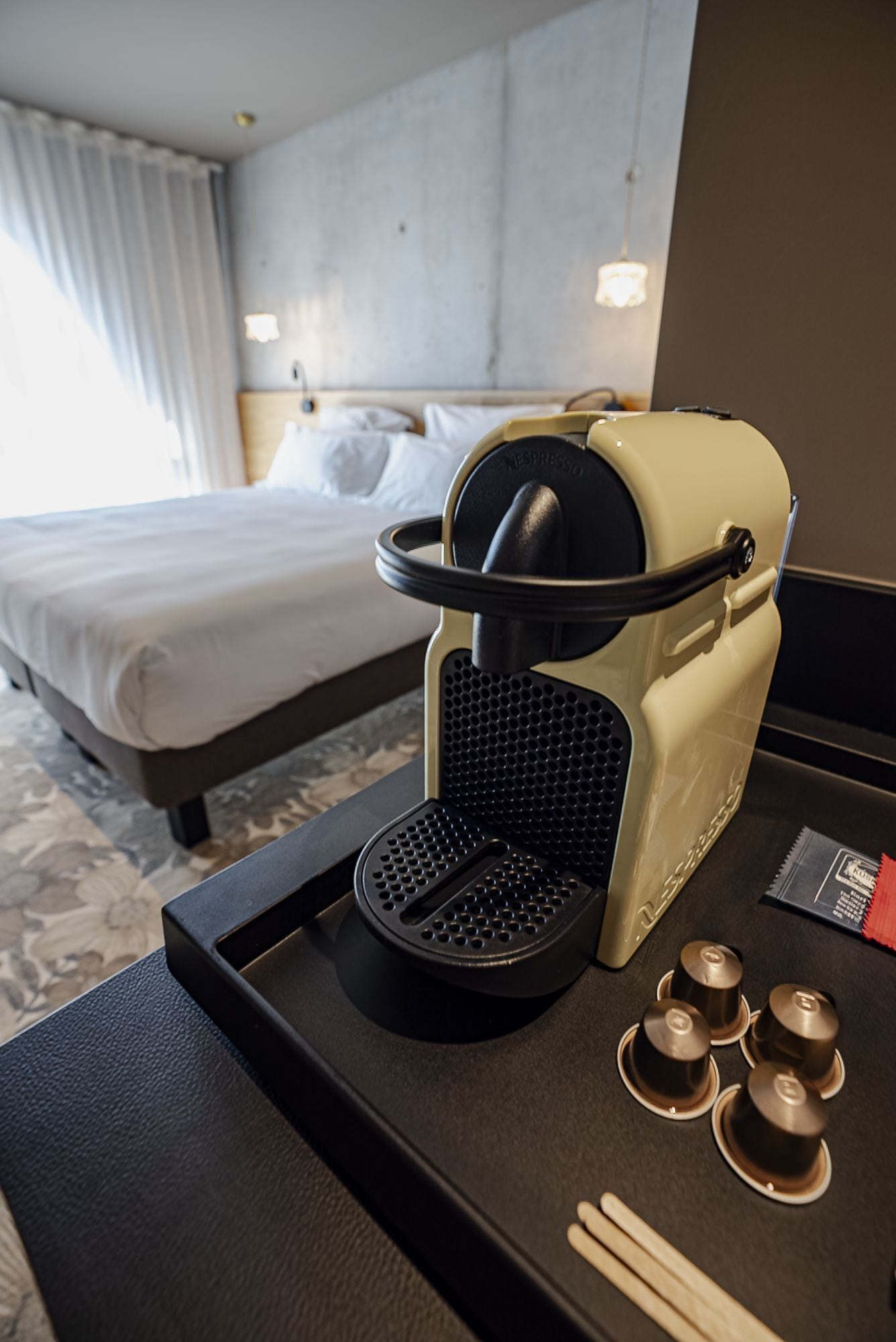 Una habitación de hotel con una cama, una cafetera y una bandeja con cápsulas de café y palillos.