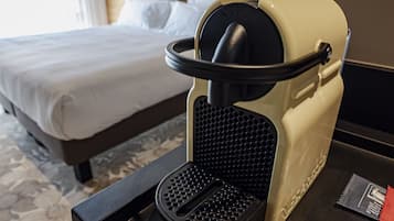 Una habitación de hotel con una cama, una cafetera y una bandeja con cápsulas de café y palillos.