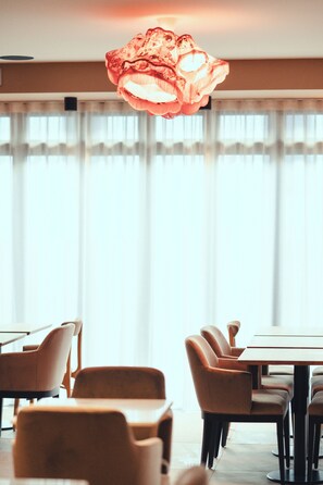 Un coin repas comprenant une table et des chaises, un luminaire suspendu et une fenêtre avec des rideaux.