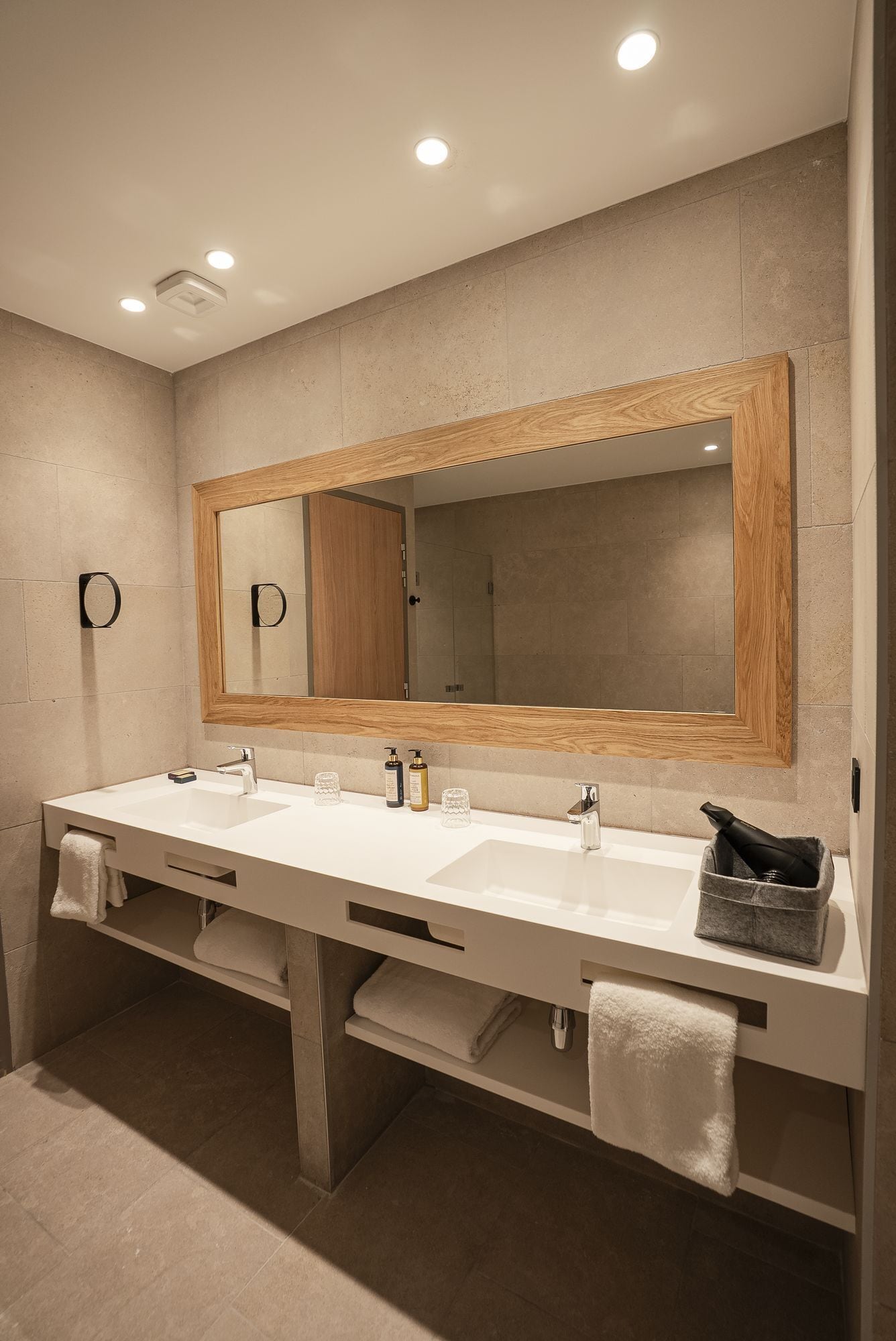 Un baño moderno con dos lavamanos, un espejo grande y luces empotradas en el techo.