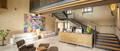 A lobby with a staircase, a reception desk, seating area, and a colorful abstract painting.