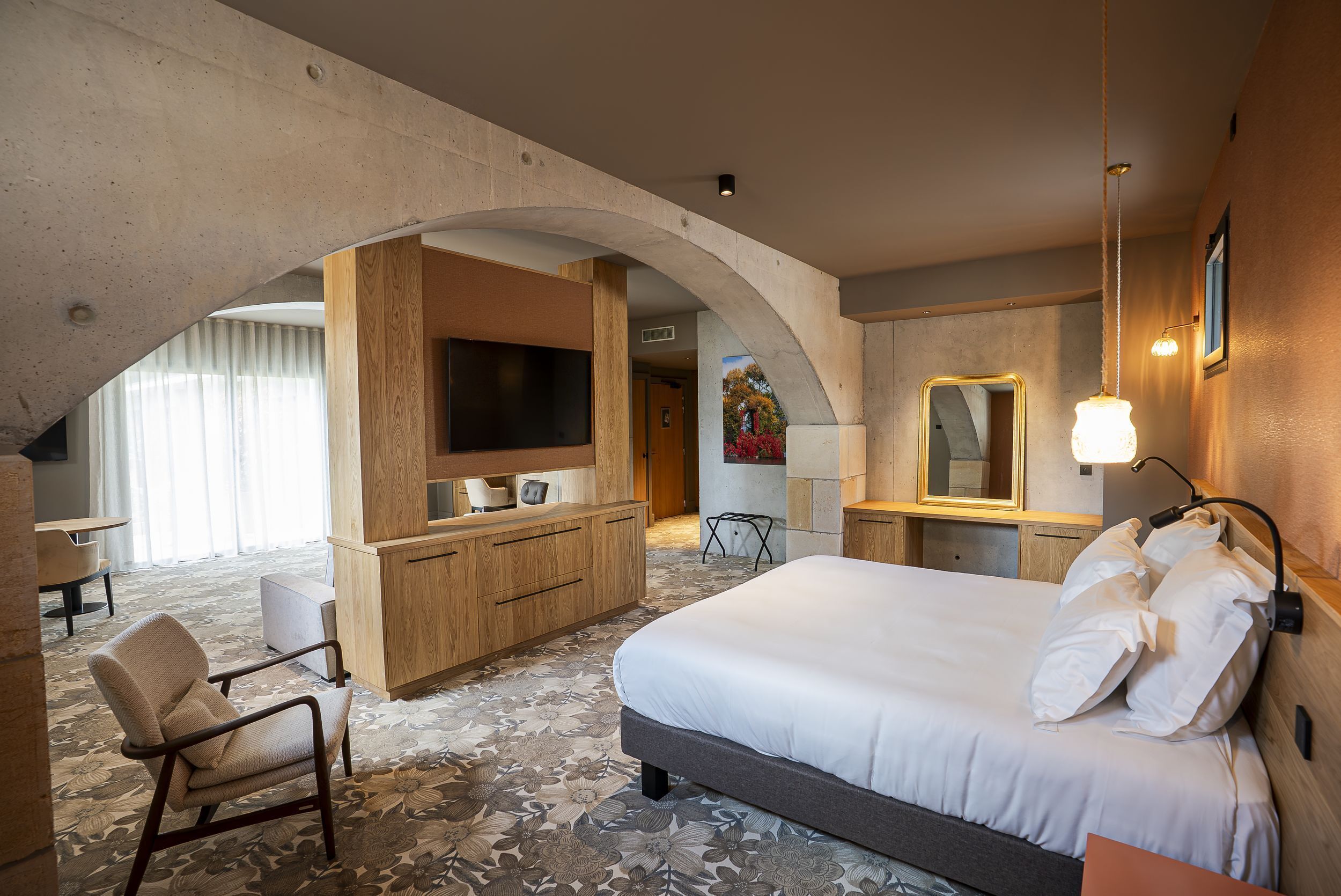 A hotel room with a large bed, a wooden desk, a television, and a mirror.