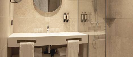 Une salle de bain moderne avec une douche à parois de verre, un miroir rond et deux lavabos avec des serviettes.