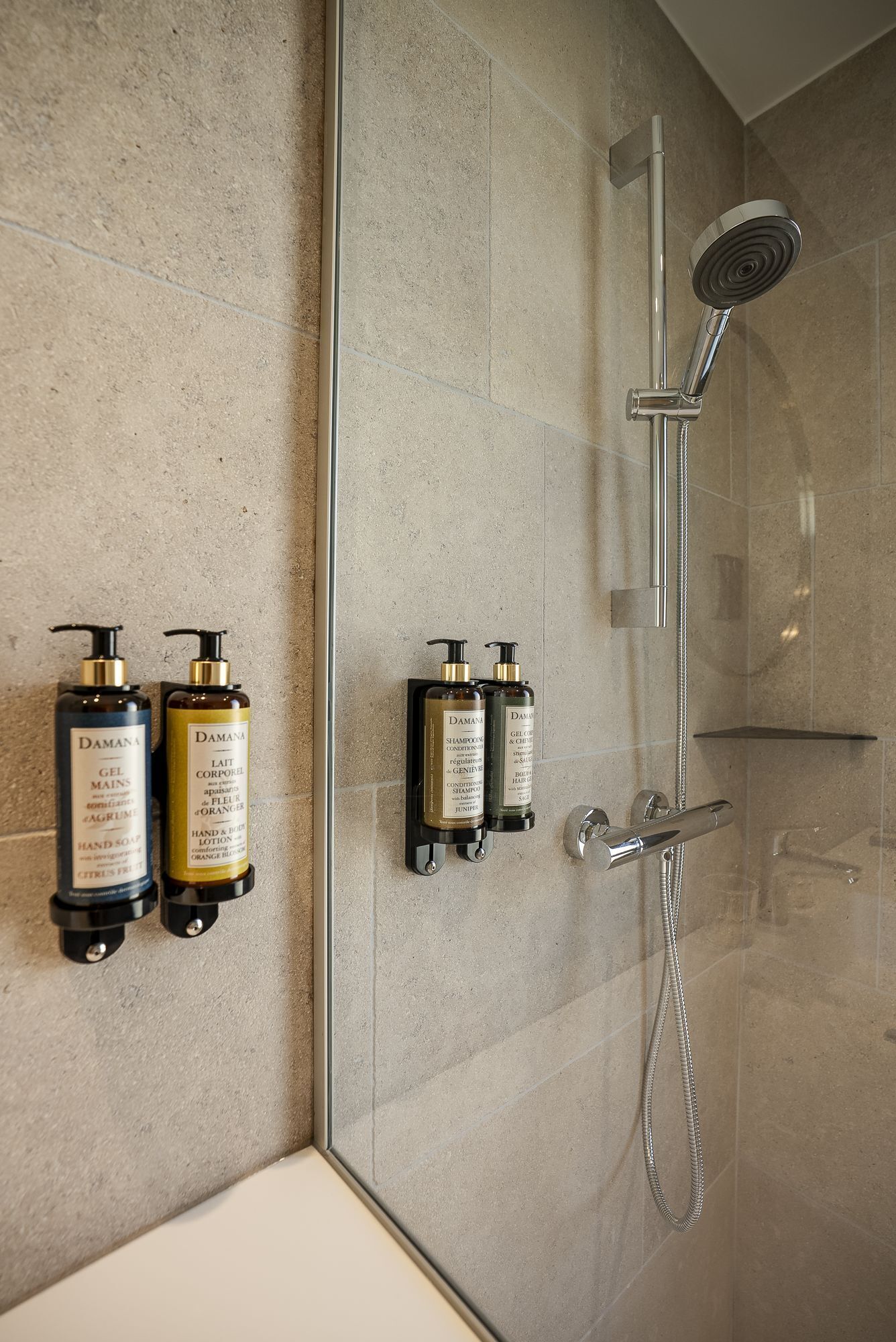 A modern bathroom with a glass shower enclosure, a handheld showerhead, and two wall-mounted shampoo and conditioner dispensers.