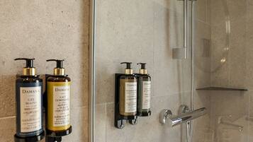 A modern bathroom with a glass shower enclosure, a handheld showerhead, and two wall-mounted shampoo and conditioner dispensers.