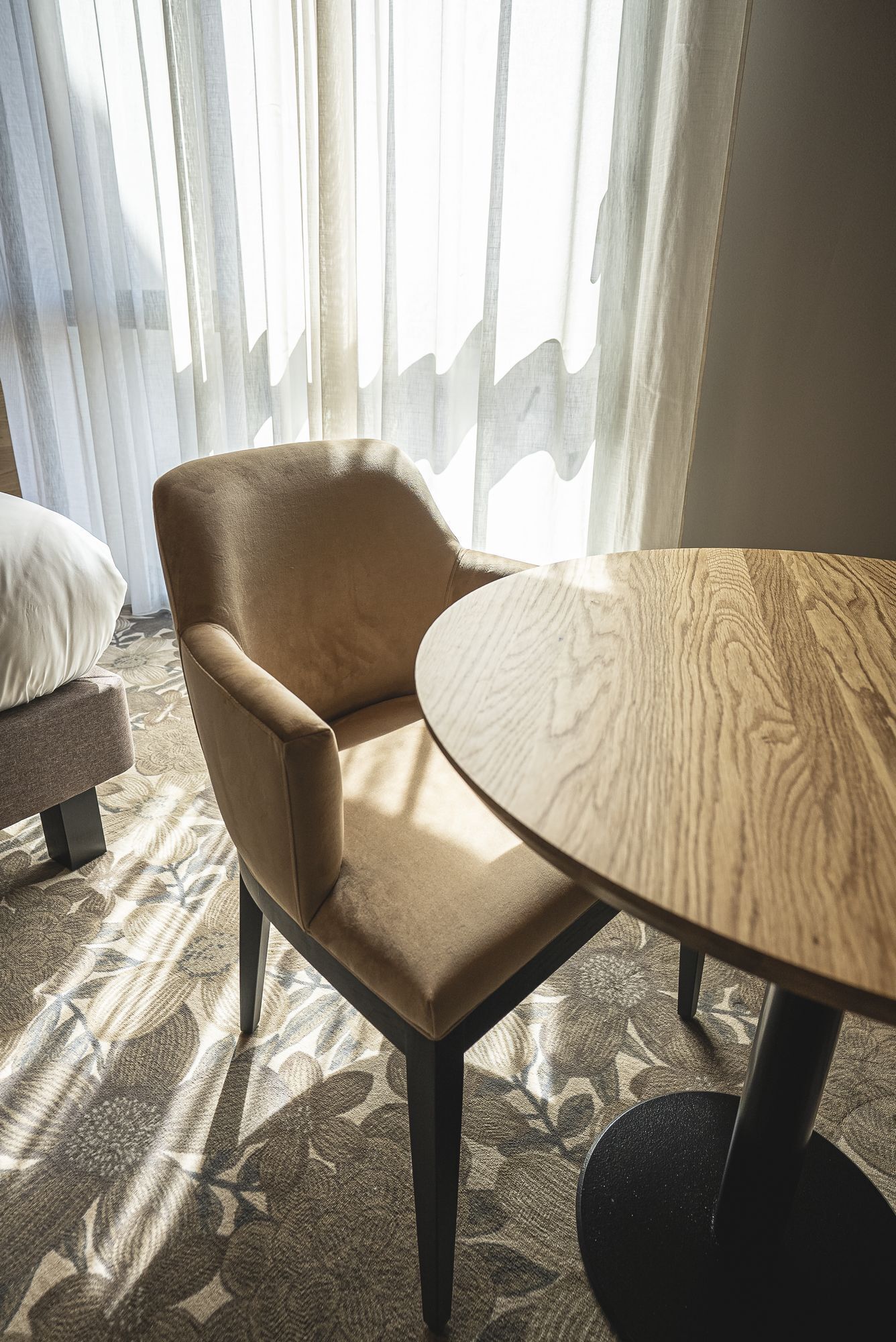 Una habitación con una mesa redonda de madera, un sillón color beige y una alfombra estampada.