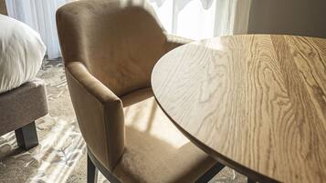 Una habitación con una mesa redonda de madera, un sillón color beige y una alfombra estampada.