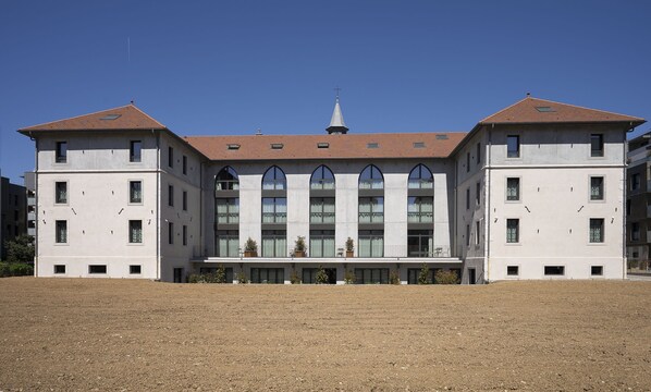 Un grand bâtiment symétrique, doté d’une section centrale avec une fenêtre en arc de cercle, d’une croix au sommet et d’un toit plat.