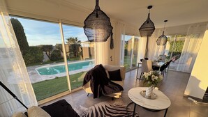Un salon spacieux doté d’une grande fenêtre, offrant une vue sur la piscine, et comprenant un coin repas.