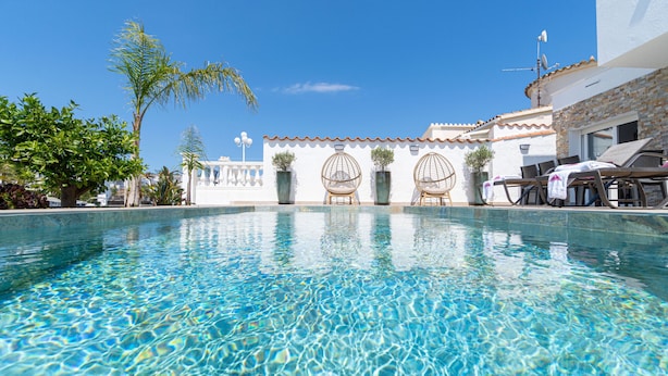 Una piscina cristal·lina amb vista a un edifici amb teulada enrajolada i parets blanques.