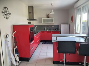 A modern kitchen with red cabinets, a built-in oven, a microwave, and a large window. - A House Between Land and Sea (Plédran)