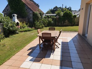 A patio with a wooden table and chairs, surrounded by a garden and a stone wall. - A House Between Land and Sea (Plédran)