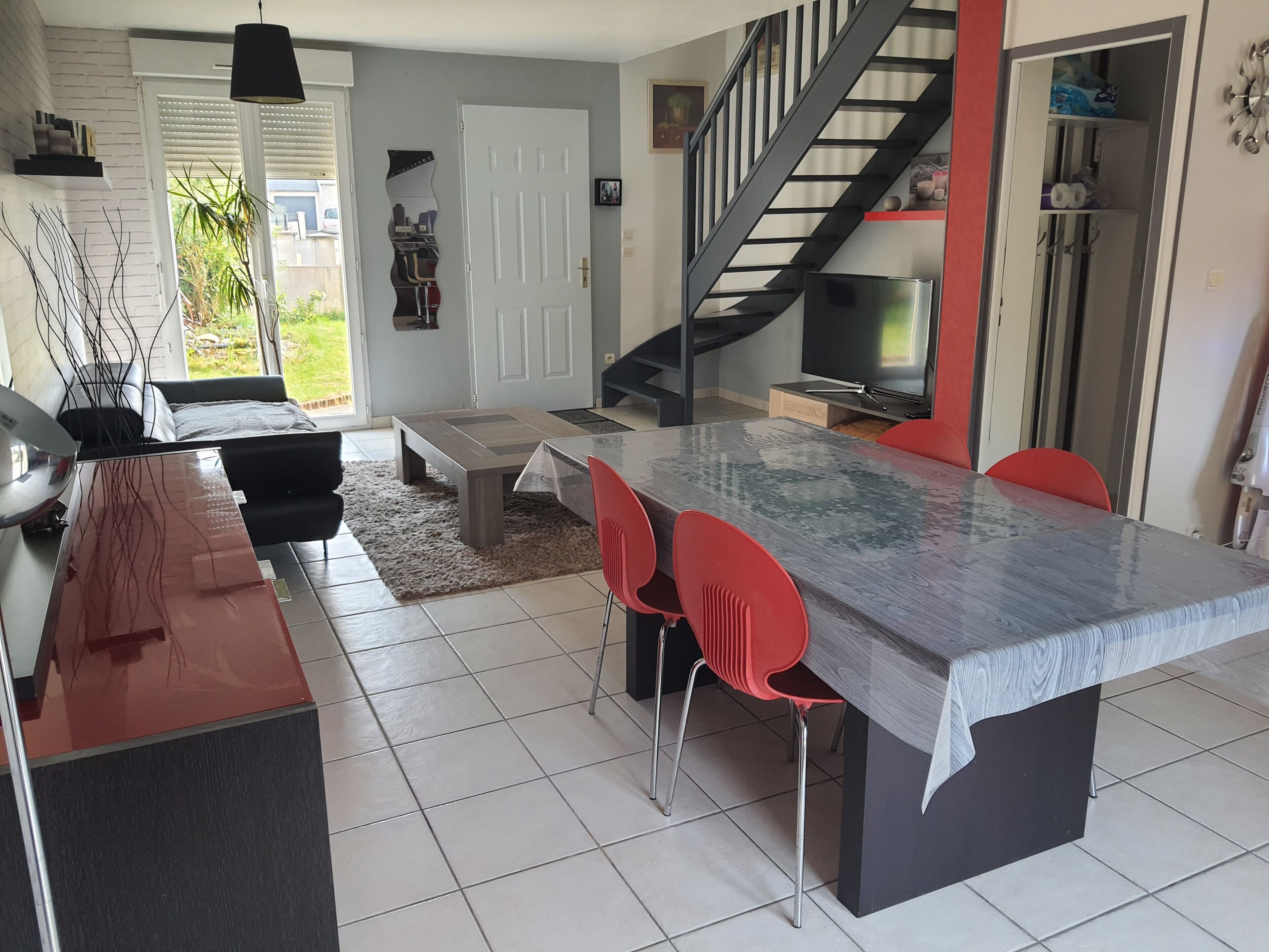 Une cuisine moderne avec un grand îlot central, des chaises rouges, un escalier et un téléviseur.