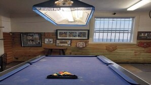 A pool table with a blue felt surface, surrounded by wooden paneling and framed pictures on the walls.