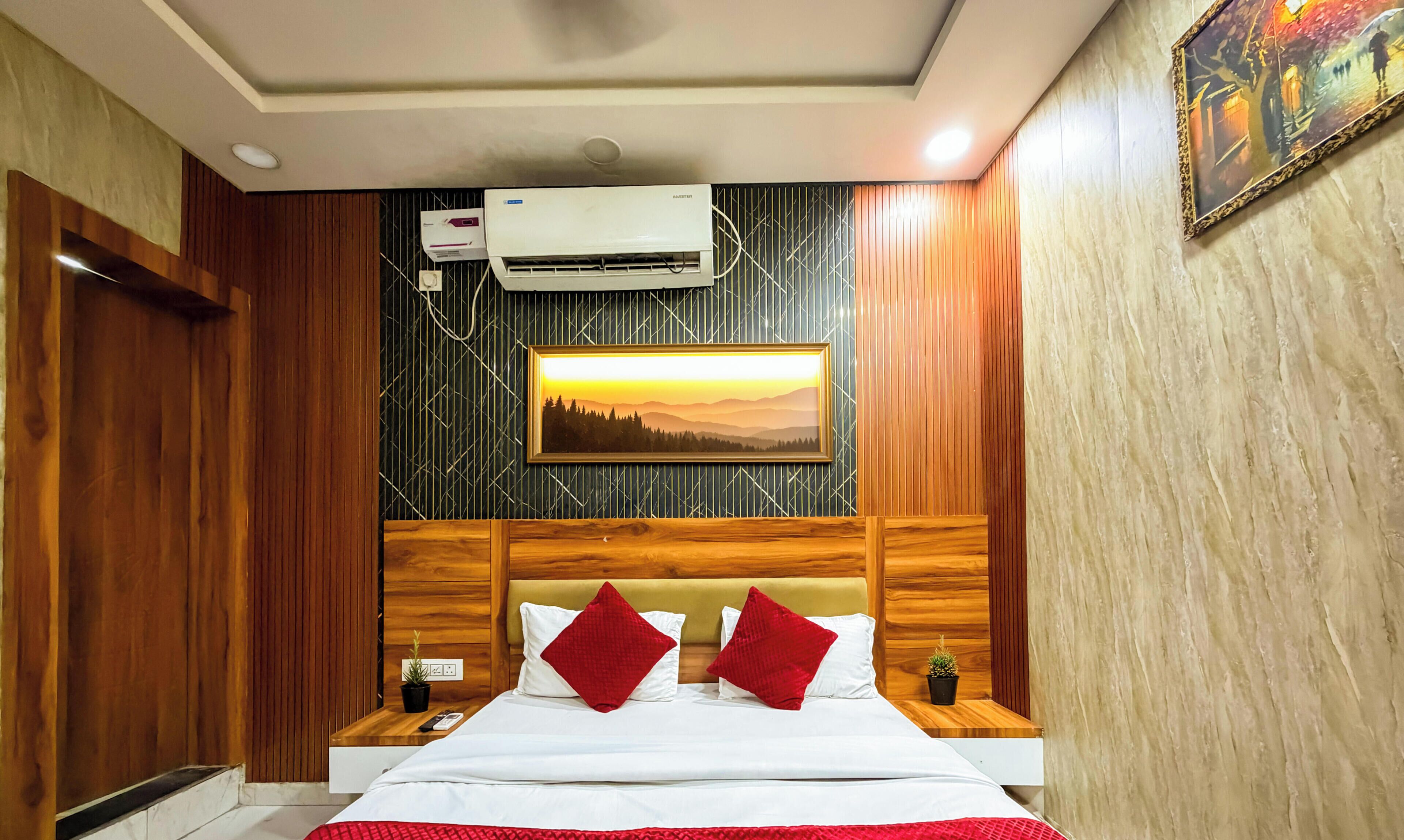 A hotel room with a bed, a nightstand, a wall-mounted air conditioner, a framed picture, and a wooden headboard.