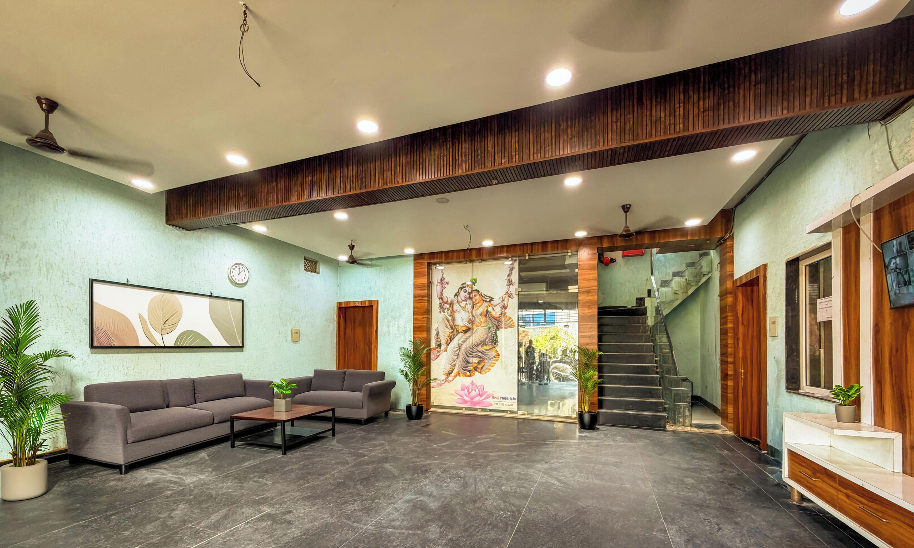 A reception area with a sofa, coffee table, potted plants, a clock, and a staircase.