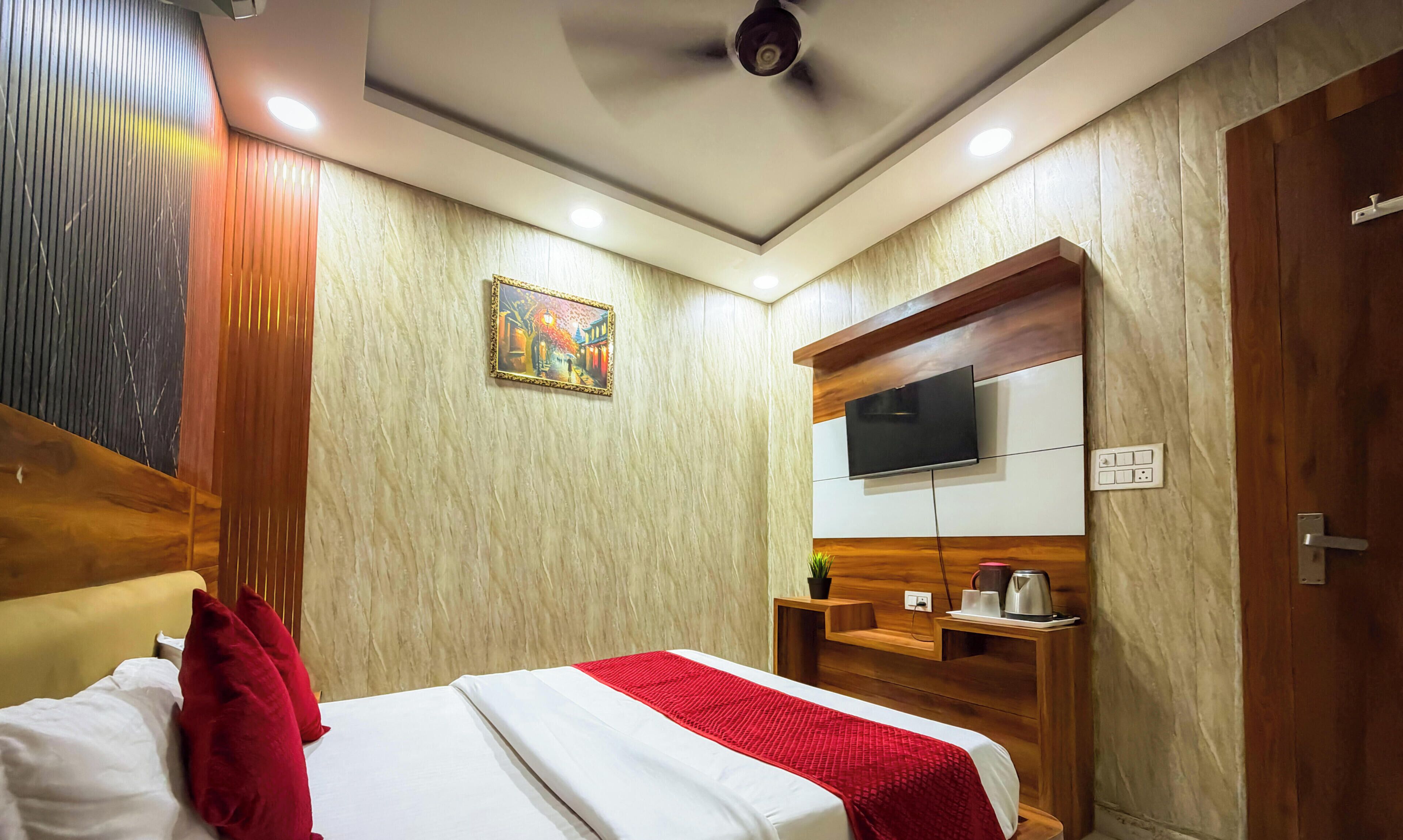 A hotel room with a bed, a TV mounted on a wooden cabinet, a ceiling fan, and a painting on the wall.