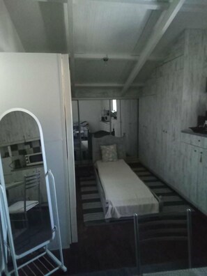 Ein kleines Zimmer mit einem Bett, einer Küchenzeile und einem Stuhl.