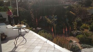 A patio with a tiled floor, a small round table, and a person standing near a grill. - Simple Stay Vari s House II (Kropia)